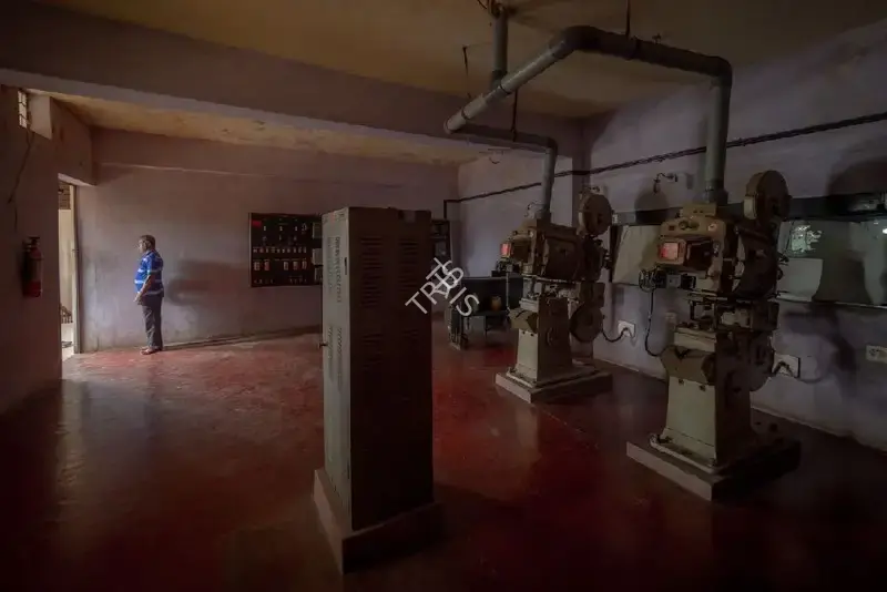 Hemant Chaturvedi (Photographer), The projectionist of Diana Talkies, Udupi, Karnataka standing alongside the projection apparatus, 2024, Contemporary Photograph